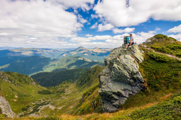 istock Hiker with a backpack standing o big stone in green rocky mounta 1157626387