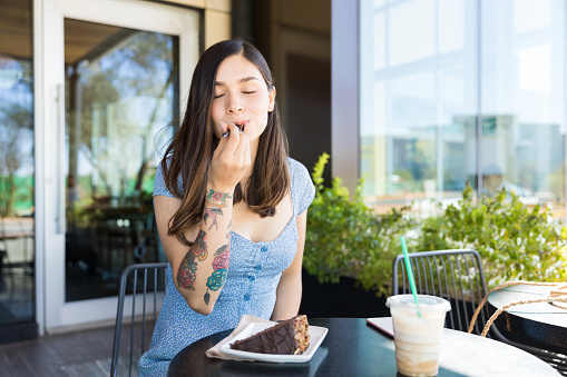 Hispanic satisfied woman enjoying pastry at cafe in shopping mall