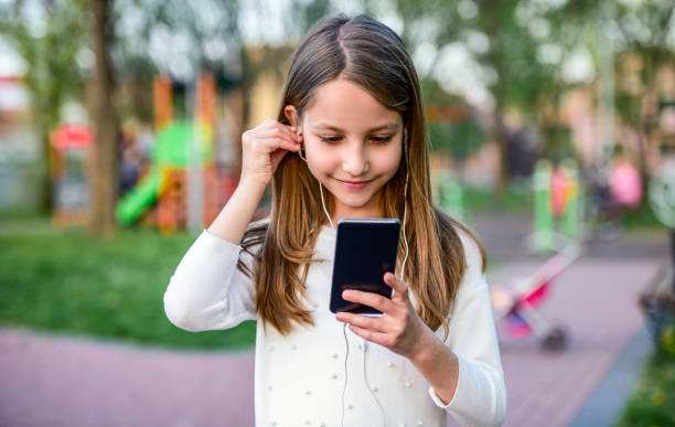 Childhood time. Cute little girl listening to music with mobile phone and headphones. Lifestyle concept stock photo