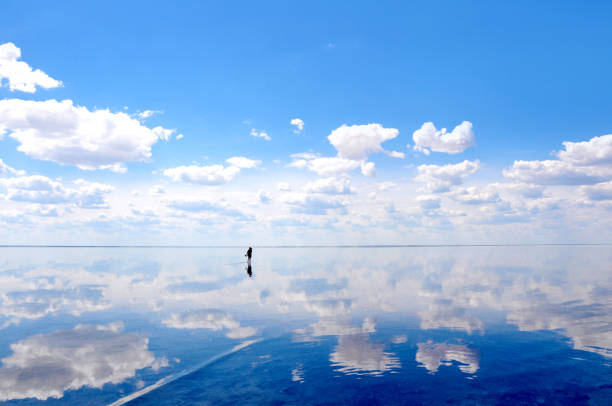 silhueta dos turistas que anda na água calma do lago elton, com reflexos surpreendentes do espelho do céu e das nuvens - andando em água - fotografias e filmes do acervo