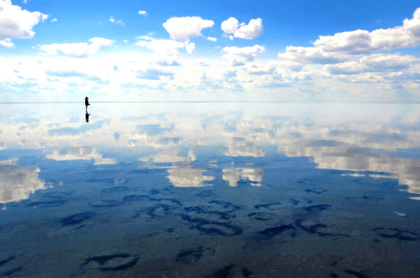 silhueta dos turistas que anda na água calma do lago elton, com reflexos surpreendentes do espelho do céu e das nuvens - andando em água - fotografias e filmes do acervo