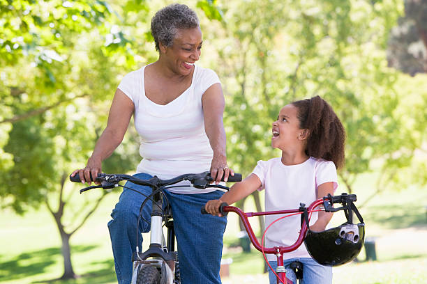 бабушка и внучка на велосипеды на улице улыбается - grandmother action senior adult grandparent стоковые фото и изображения