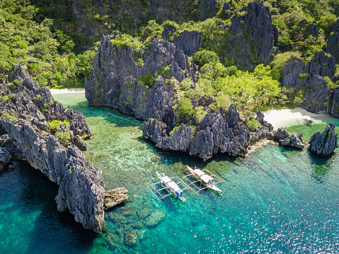 Aerial view towards the beautiful natural Hidden Beach Lagoon at Matinloc Island with typical Balangay Tourist Tour Boats anchored in front of the rock formations from where you can swim into the beautiful natural rock lagoon and small beach. Aerial Drone Point of View. Hidden Beach, Matinloc Island, Mimaropa, El Nido, Palawan, Philippines, Asia