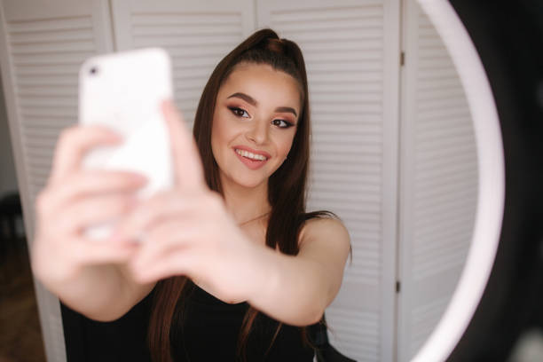 istock Young attractive model make a selfie after makeup in beauty studio. She use a ring lapm for photo. Background of white folding screen 1157712787