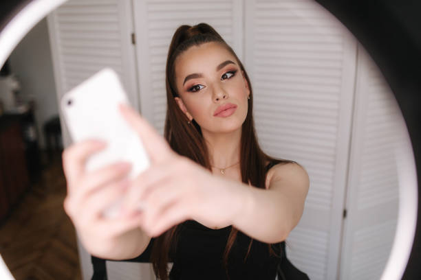 istock Young attractive model make a selfie after makeup in beauty studio. She use a ring lapm for photo. Background of white folding screen 1157712797