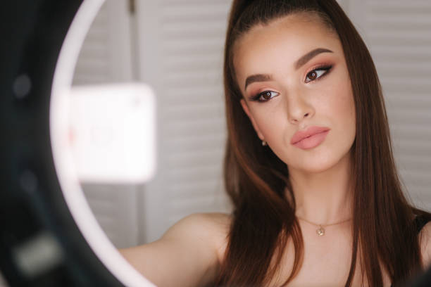 istock Young attractive model make a selfie after makeup in beauty studio. She use a ring lapm for photo. Background of white folding screen 1157712813