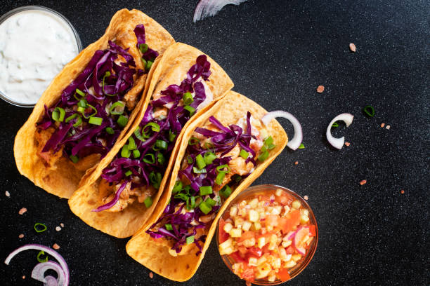 traditionelle mexikanische tacos mit huhn, gegrilltem gemüse, zwiebeln und lila kohl, serviert mit weißer und roter sauce und zwiebelringen. ansicht von oben. dunkle hintergrund. kopierraum - grilled chicken chicken corn salsa stock-fotos und bilder