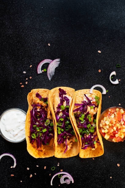 traditionelle mexikanische tacos mit huhn, gegrilltem gemüse, zwiebeln und lila kohl, serviert mit weißer und roter sauce und zwiebelringen. ansicht von oben. dunkle hintergrund. kopierraum - grilled chicken chicken corn salsa stock-fotos und bilder