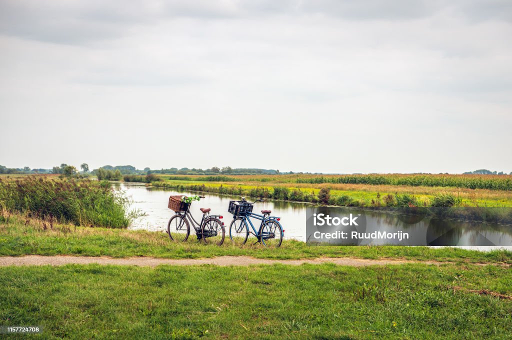 Women's and men's bicycle parked along the water of a stream Women's and men's bicycle, each with a basket on the handlebars,  parked along the water of a stream in a Dutch polder. The owners are not visibly present in the area. Cycling Stock Photo