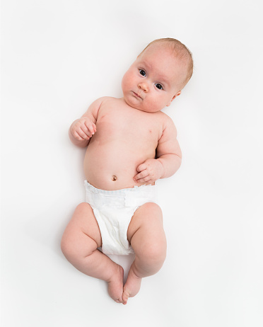 A cute four month old baby girl wearing a white diaper cover lie down on white background