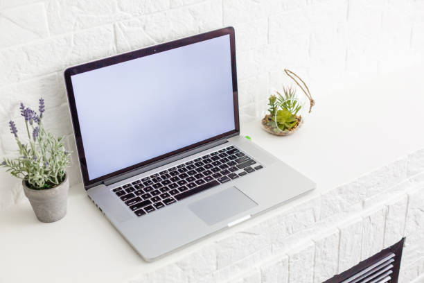 Laptop with blank screen on white table with mouse and smartphone. Home interior or office background