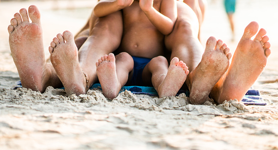 Unrecognizable family lying at the beach with sandy feet. Focus is on feet.