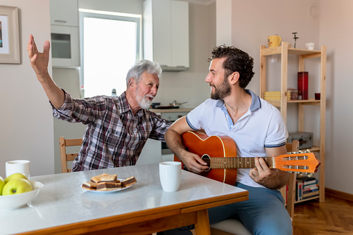 Adult Son Playing Guitar for His Senior Father at Home. Happy Family Concept. Musician at Home. Music and Songs Concepts.