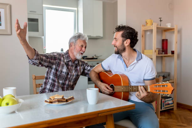 Adult Son Playing Guitar for His Senior Father Adult Son Playing Guitar for His Senior Father at Home. Happy Family Concept. Musician at Home. Music and Songs Concepts. father and son guitar stock pictures, royalty-free photos & images