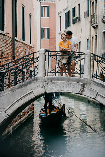 This is an image of a traditional gondola being punted by a traditional gondolier going under one of the many canal bridges in Venice