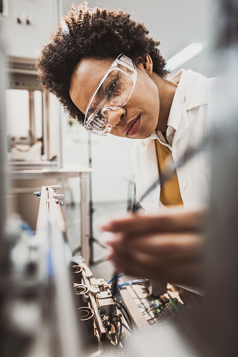 African American lab worker examining machine part while working in a lab.