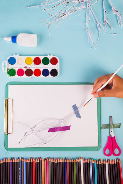 istock The hand with a brush paints branches in white on clipboard. 1157746583