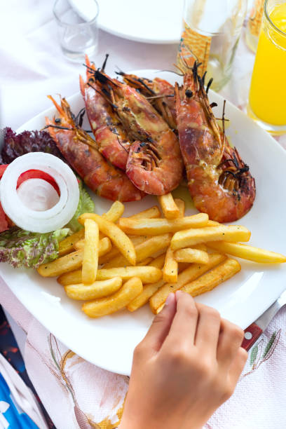 istock Hand boy eating shrimps seafood and fried potatoes at dinner table by self. 1157746596
