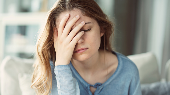 Poor young Caucasian woman sitting on sofa touching her nose having sinus problems