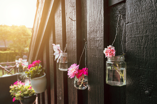 Old glass jar is connected to a metal wire and hang on a wall outside. There are water and flowers in the jar. Concept of upcycling where old products are reused and turned into something useful insted of being thrown out.