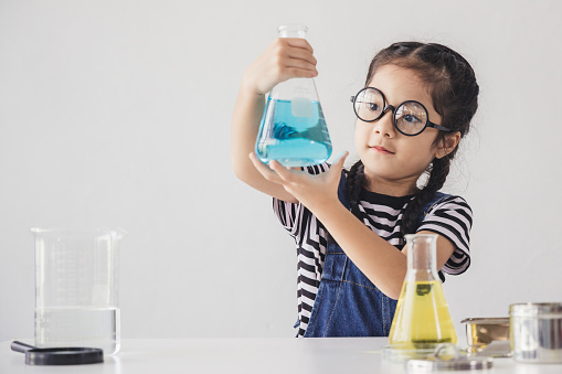 Education concept - Little scientists children is looking at erlenmeyer flask containing chemicals to perform experiments in the laboratory, Beaker on the side table.