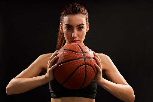 Portrait of young charming player holding basketball ball while standing against plain background