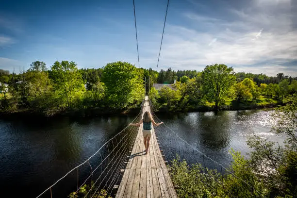 Photo of Woman crossing a suspension footbridge in Quebec.