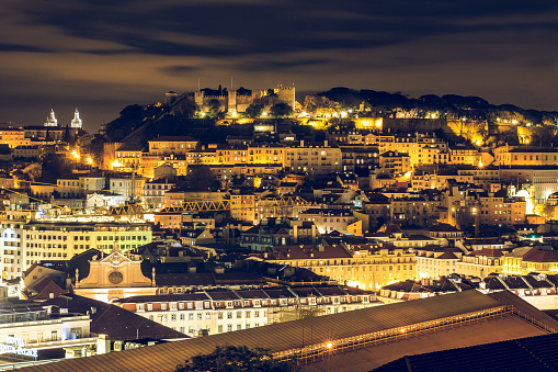 Lisbon at night. The capital of Portugal with the castle Sao Jorge from the lookout point. Illuminated skyline at night with buildings and roofs