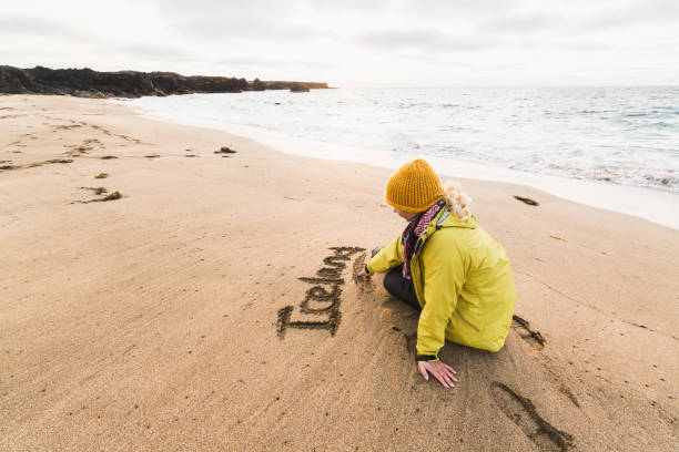 chica con impermeable amarillo escribiendo la palabra islandia en la arena de la playa de skardsvik al atardecer, península de snaefellsnes - snaefellsnes fotografías e imágenes de stock