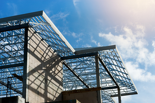 Metal roof frame structure of a two story house without  roof tiles under sunny cloud blue sky,low angle view.