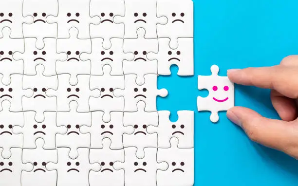 Photo of Hand of a businessman chooses a smiley face on piece of white jigsaw puzzle on blue background, The best excellent business services rating customer experience, Satisfaction survey concept