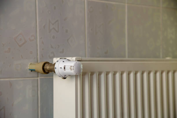 istock Heating radiator with thermostat valve on light wall tiles copy space background. Comfortable warm home interior, climate control, money saving concept. 1157764118