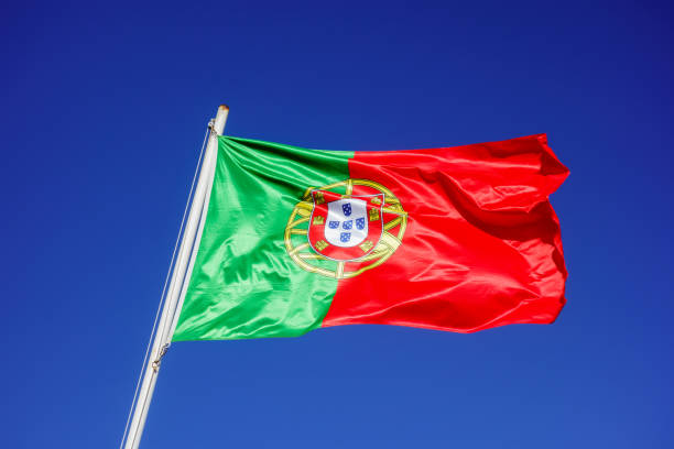 Flag of Portugal flapping in wind against empty blue sky.