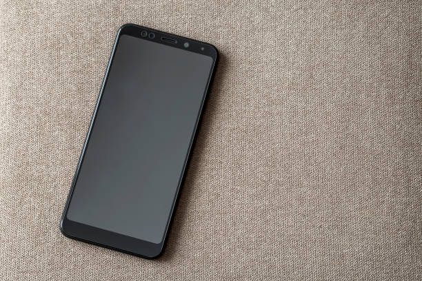 istock New black modern cellphone isolated on light cloth copy space background. Modern technology, communication and gadget design concept. 1157766370