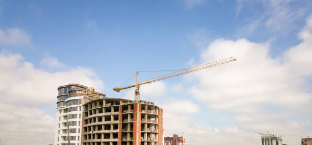 istock Apartment or office tall building under construction. Brick walls, glass windows, scaffolding and concrete support pillars. Tower crane on bright blue sky copy space background. 1157766518