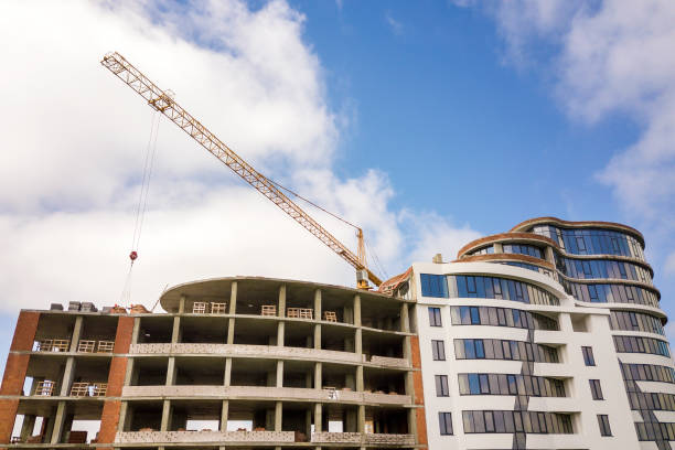 istock Apartment or office tall building under construction. Brick walls, glass windows, scaffolding and concrete support pillars. Tower crane on bright blue sky copy space background. 1157766533