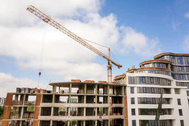 istock Apartment or office tall building under construction. Brick walls, glass windows, scaffolding and concrete support pillars. Tower crane on bright blue sky copy space background. 1157766538