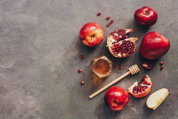 Photo of Apples, pomegranate and honey on a dark rustic background. New Year - Rosh Hashana. Traditional Jewish food. Top view, copy space, flat lay