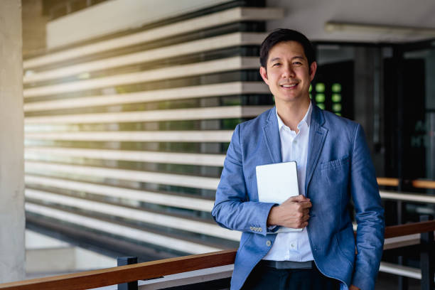 portrait of asian business man with digital tablet at outdoors over office building in background - businessman one man only standing elegance imagens e fotografias de stock