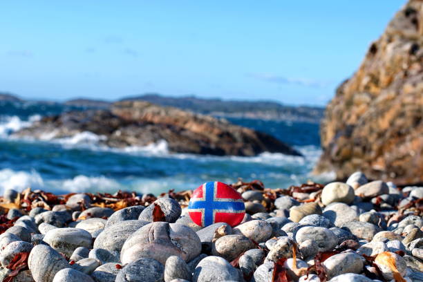 Image of the flag of Norway on a stone, between sea pebbles and seashells. Concept of Norwegian Constitution Day.  Celebrated on May 17.