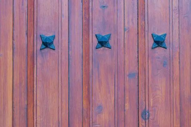 Photo of Wooden texture background. Closeup of a detail from a wooden red brown entrance door with three metal stars on the wooden planks. Macro.