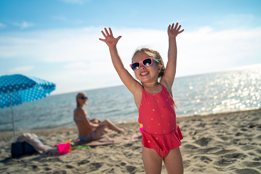 Portrait of smiling girl standing on the beach with raised hands.