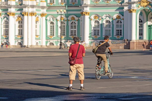 St. Petersburg, Russia - June 22, 2019:  tourists walk on the Palace Square near the Hermitage. Man riding a folding bike