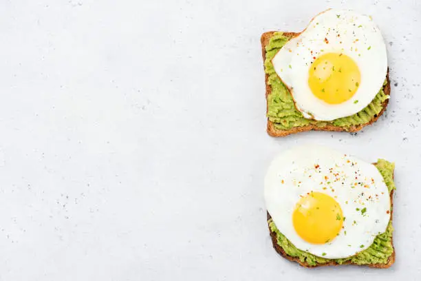 Toast with mashed avocado and sunny side up egg on grey concrete background. Table top view, healthy food, clean eating concept