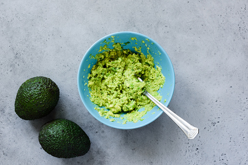Mashed avocado in bowl on grey concrete background. Table top view. Cooking healthy vegan or vegetarian sauce or dip