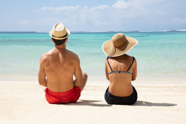 istock Couple Wearing Hat Sitting On Sand Looking At Sea 1157815152