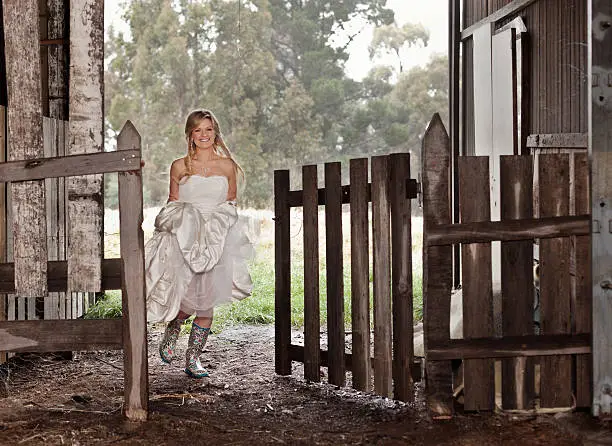 Beautiful young bride running through gate wearing bright colorful rubber boots