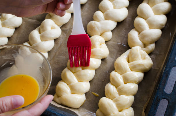 istock Preparation process - raw unbaked buns. Female hand lubricates raw buns with an egg before baking. 1157838976