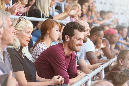 Man smiling while sitting on stadium among crowd.
