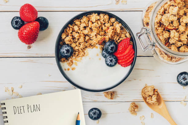 istock Homemade granola and fresh berries on wood table with note book and text diet plan concept, copy space. 1157854507